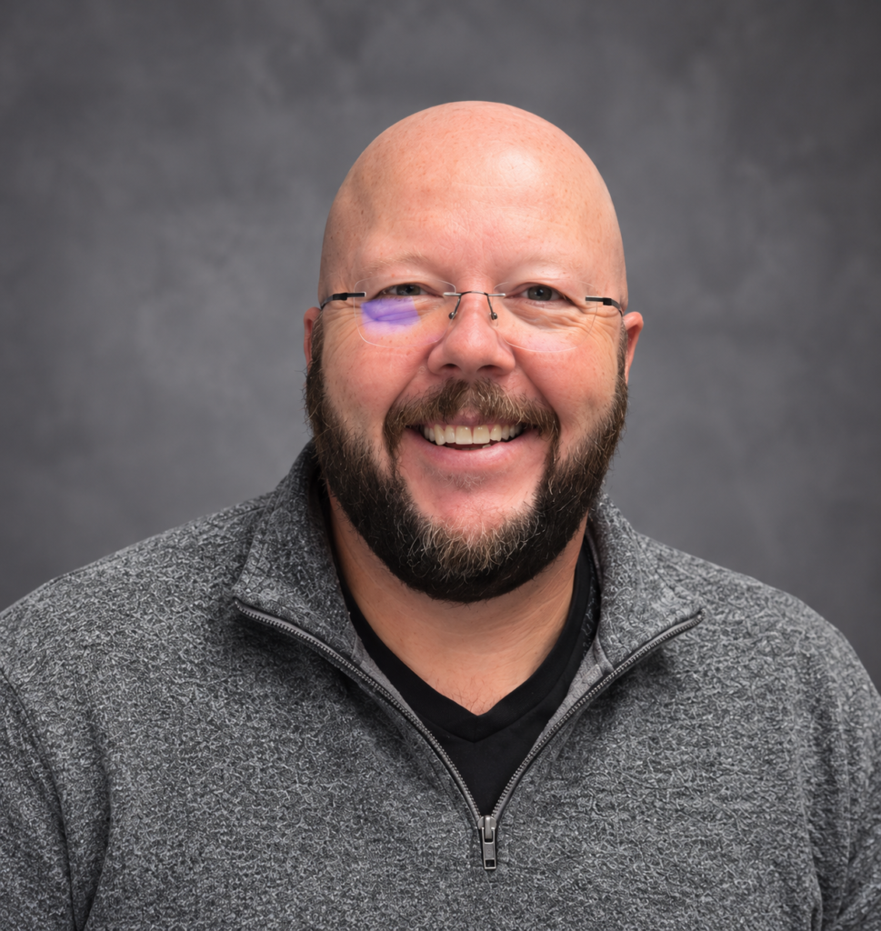 Smiling bald bearded man with glasses wearing a gray fleece jacket