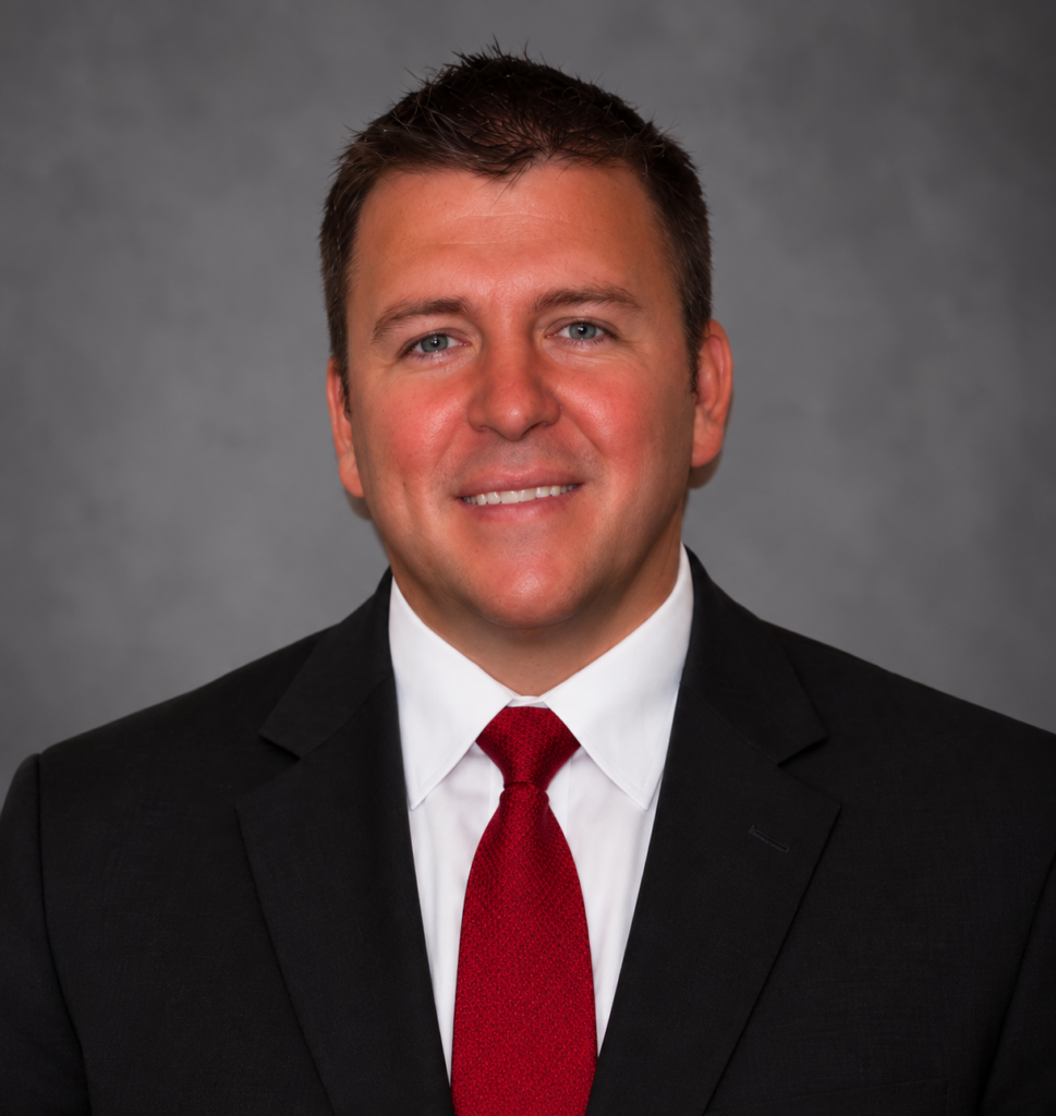 Professional headshot of man in dark suit with a red tie