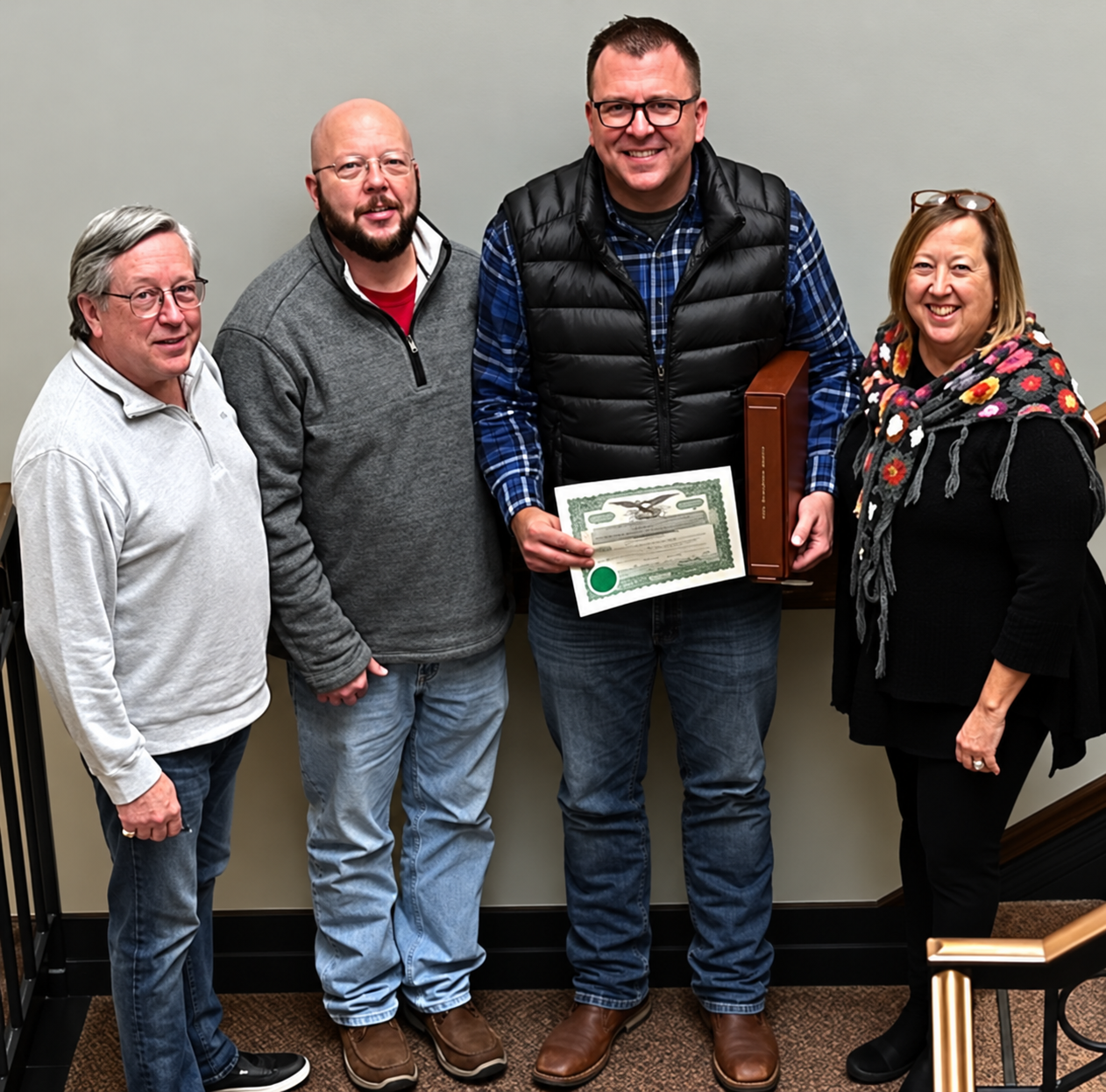 Four adults standing together indoors while displaying a framed award
